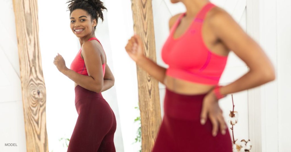 Woman looking in the mirror happy with the results of her body contouring treatment (MODEL)